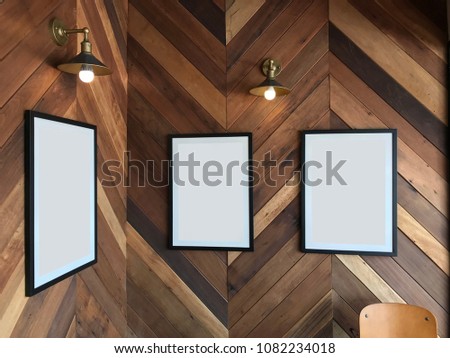 Three empty black frame on the vintage wood wall, with classic lamp on top