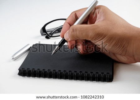 hand holding pen to write on a black book 