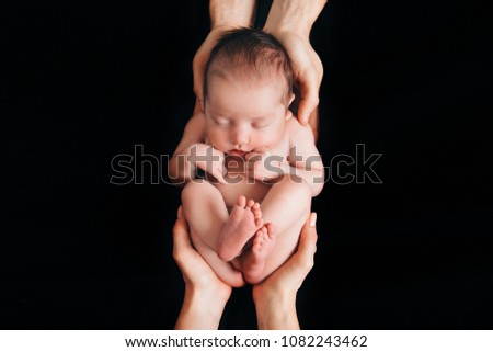 newborn baby lying on the hands of parents on a black background. Imitation of a baby in the womb. beautiful little girl sleeping lying on her back Royalty-Free Stock Photo #1082243462