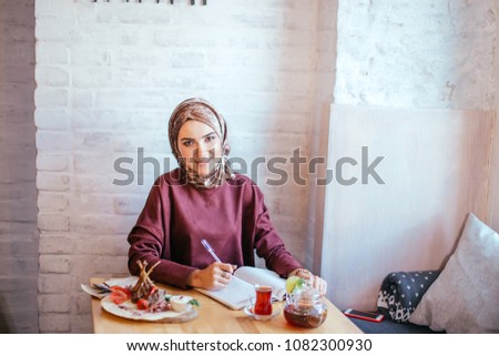 Muslim woman writing love diary in cafe