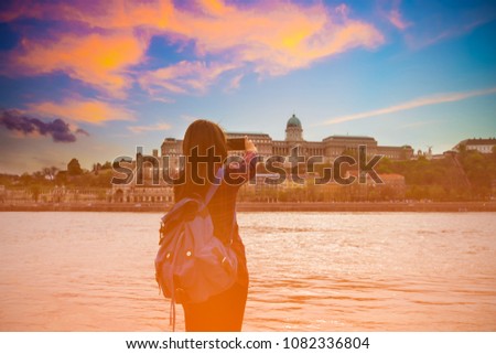 Rear of young woman with backpack take a picture at Panoramic view of sunset which  one of the most beautiful cities in Europe- Budapest,  Hungary.
