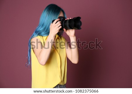 Young female photographer with camera on color background