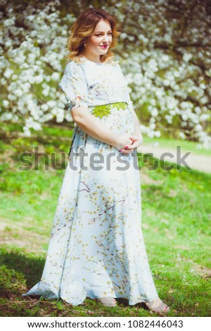 Beautiful blonde pregnant woman walking in the green garden