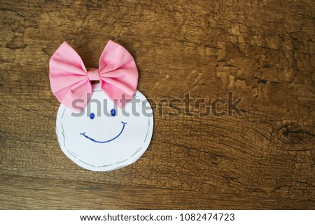 A smiling face drawing picture with pink bow on the wood floor background.