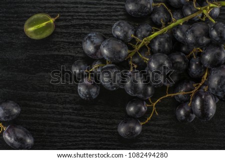 Black grape clusters (autumn royal variety) with one sliced berry table top isolated on black wood background
