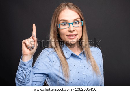 Business lady wearing blue glasses posing having idea showing index finger on black background
