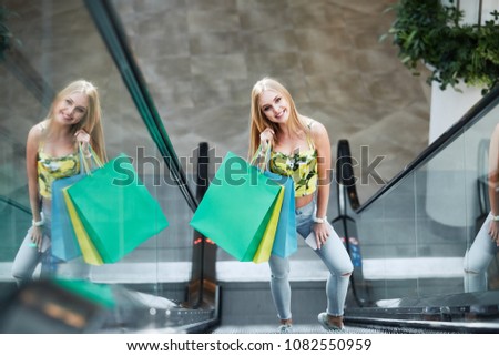 Attractive blonde girl posing with colorful shopping bags at shopping mall background during shopping process and smiling, shopping concept, portrait.