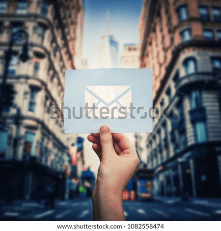 Woman hand holding a paper sheet with envelope message icon over city street background. Big city life new email incoming message. Bussiness social network.