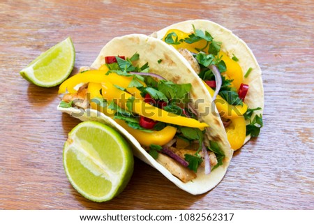 Mexican tacos with grilled chicken fillet, fresh vegetables and lime on rustic wooden background. Side view, closeup. 