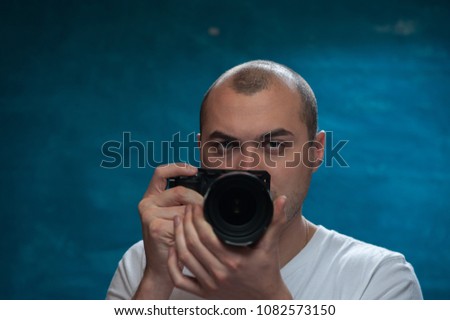 Male professional photographer posing with camera against blue background