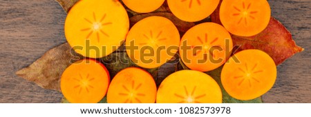 Persimmon fruits, cut in half, on persimmon leaves background, top view banner