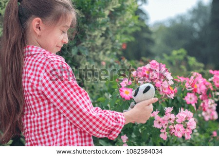 A girl with a smiling face is holding a small panda toy. The concept of childhood. Natural sunlight. Selective focus