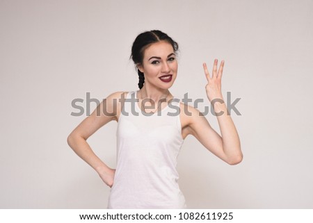 portrait of a beautiful brunette girl in a T-shirt on a gray background showing a thumbs digit. She stands right in front of the camera and smiles and looks happy.
