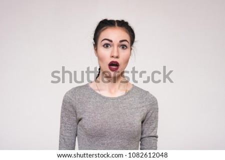 impressive female emotions. Portrait of a beautiful brunette girl on a gray background showing her emotions. She is standing right in front of the camera and she likes what she does