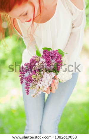 beautiful woman with red hair holding white and violet lilac bloom in her hands, outdoor garden, can be used as background