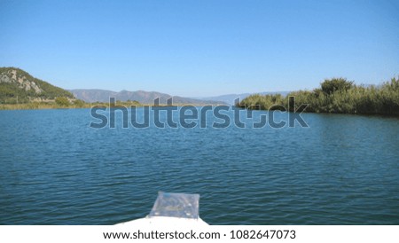 Beautiful view from the bow of moving ship along bay on sunny day. Sailboat floating on river with blue sky and mountain landscape at background. Concept of summer vacation or holiday. Close up.