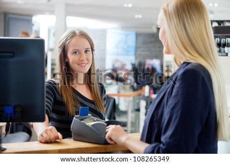 Portrait of young female sales clerk standing by counter with customer at parlor