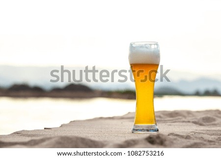 Glass of beer on the sand with river background, copy space on the left