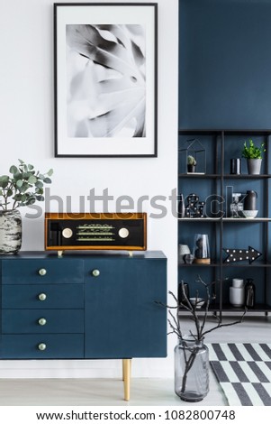 Close-up of a painting, blue cabinet, retro radio and glass vase with branches in dark living room interior and metal shelf in the background Royalty-Free Stock Photo #1082800748