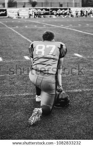 The player of the American football team kneels near the playing field.