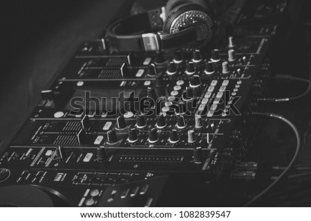 Closeup of dj musical mixer professional console black color with many buttons and knobs and glamour headphones with pastes in night club or studio, horizontal picture