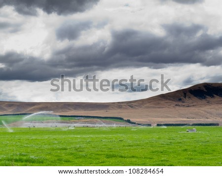 Turning a dry mountain valley into lush green farm pastures by irrigation with a long mobile sprinkler system while livestock graze peacefully nearby Royalty-Free Stock Photo #108284654