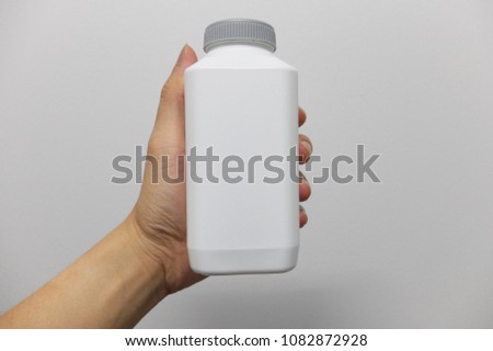 A Hand Holding a White Opaque Plastic Bottle on a White Background