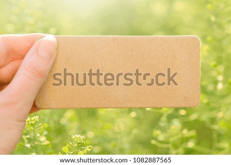 Hand holding empty card on green summer background.