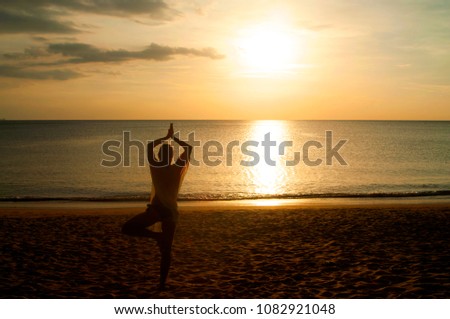 Young woman  practicing yoga on the sea beach at sunset, Thailand