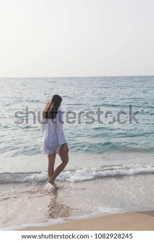 Back view of a young woman in a white beach outfit, walks on the beach. Travel & Summer vacation concept