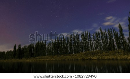 Night photography at a river with a line of trees is reflected on the water. Some stars and clouds in the sky Blue hour. Patagonia, Argentina