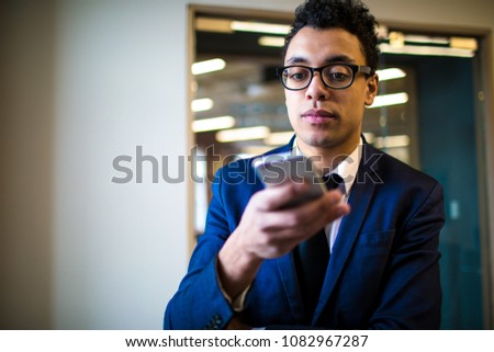 Serious man CEO in suit and glasses using applications on mobile phone standing in office near copy space. Thoughtful male leadership watching video in internet via smartphone. Online payment 