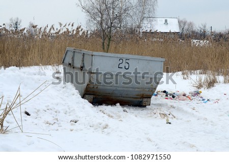 Trash bin at the side of street in winter with lip garbage container winter snow. Metal container for household waste