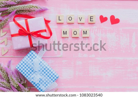 Happy mother's day concept. Top view of gift box with flower and tag with Love you MOM text on wooden block with pink handmade heart on on pastel color bright pink and white wooden background.