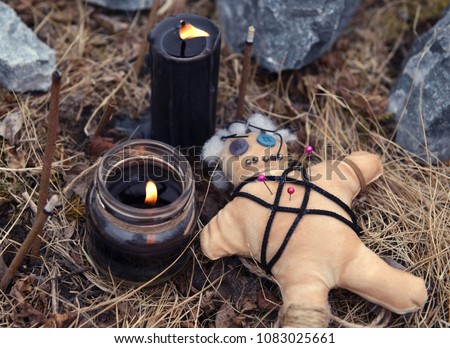 Voodoo doll with burning black candles and incense sticks among stones. Mystic background with ritual esoteric objects, occult and halloween concept