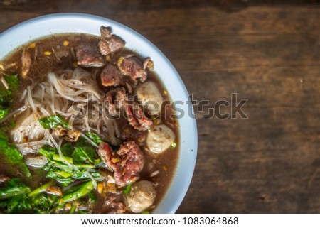 Soft Focus,Small noodles in a white bowl are placed on the wooden table in a clear view of the ingredients inside the dish. Beef and meatballs are topped with broth to add flavor to the noodles.