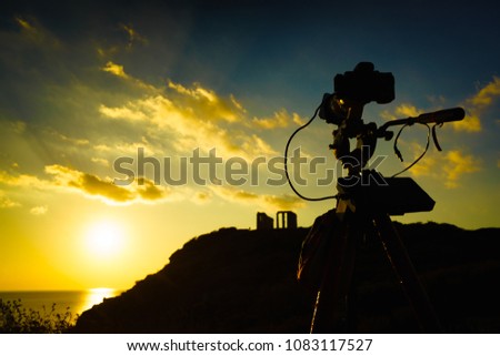 Greece Cape Sounion. Professional camera on tripod taking picture film video from ruins of an ancient temple of Poseidon at sunset. Travel destinations.