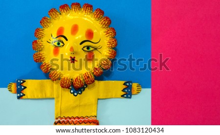 Mexican handicraft, hand painted doll representing the sun, on a colorful paper background.