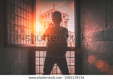 Man photographs cathedral in Pisa through the bars on the window at sunset