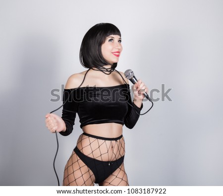 expressive brunette woman with microphone in shorts and net stockings.