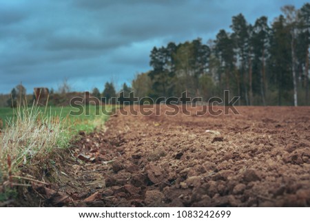 Tilled crop fields in a cloudy spring day. Texture in a freshly tilled soil surrounded by nature in bloom. Cultivated farm land in a vast territory.  Stormy weather in country side. 