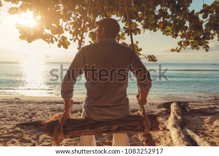 Man sitting on the wooden swing and enjoying the ocean.