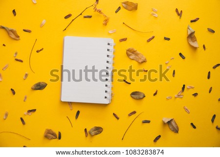 Blank notebook and dry leaves on yellow paper background for top frame