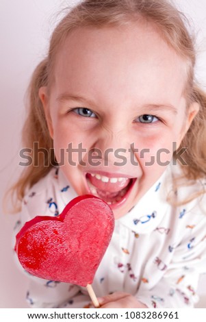 Cute happy little girl with lollipop in heart-shaped red candy with copyspace