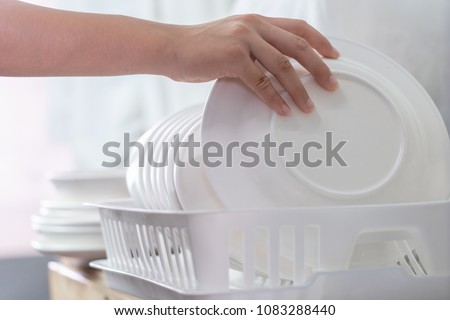 Hand of woman putting just washed clean plate in the dish rack Royalty-Free Stock Photo #1083288440