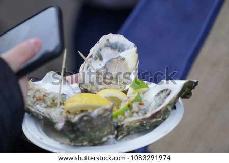 Fresh raw Oysters with lemon on plate in hand holding and smartphone for take a picture at seafood market. in Borough Market,London.