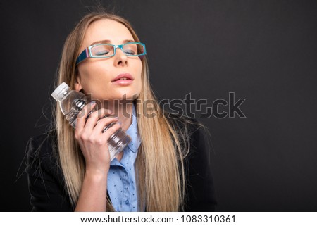 Business lady wearing blue glasses cooling with bottle of water on black background with copyspace advertising area