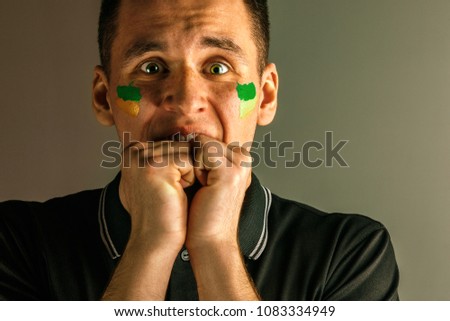 Portrait of a man with the flag of the Brazil painted on him face. Young male caucasian model closeup. Football, soccer, fan concept. Human emotions, facial expressions concepts
