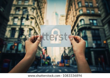Woman hands holding a paper sheet with lock symbol in the middle of the street in a big city. Padlock as security symbol in business. Data privacy protection concept.