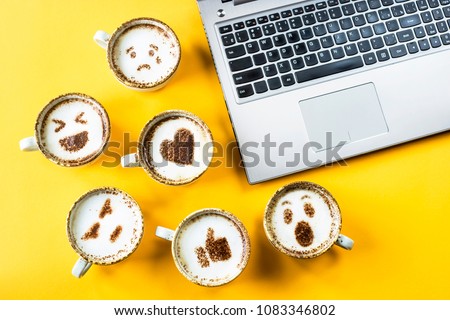 Smile emoji painted on cups of cappuccino next to the laptop on a yellow background. Emotions and communication online concept Royalty-Free Stock Photo #1083346802